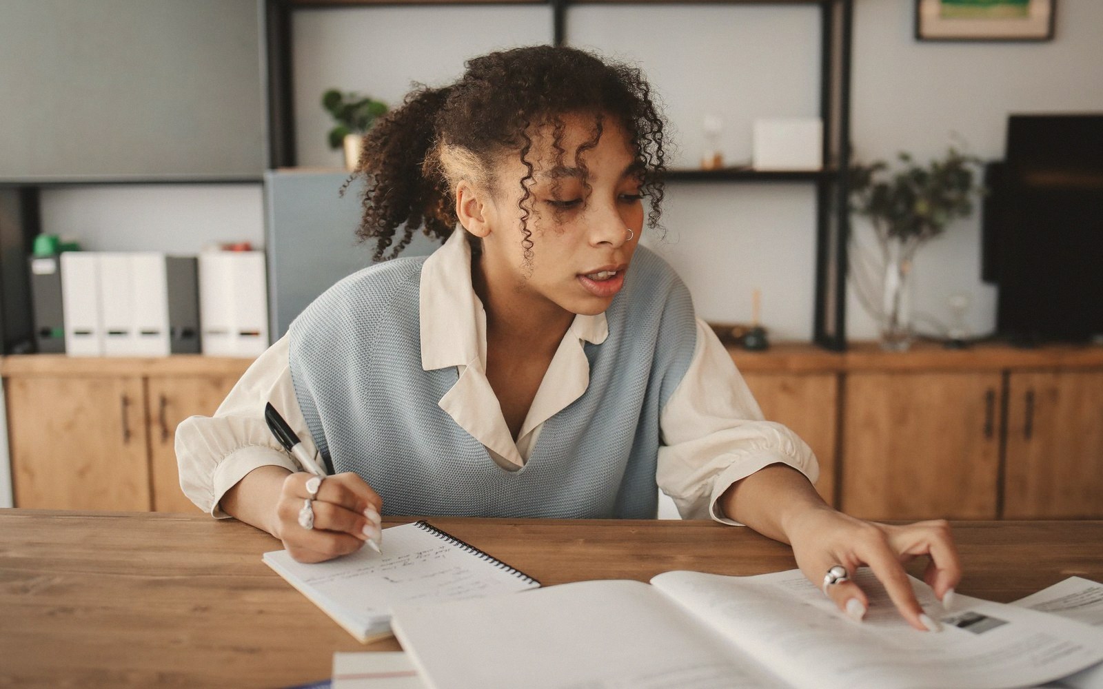 Woman writing in a notebook while reading from an open textbook at a desk