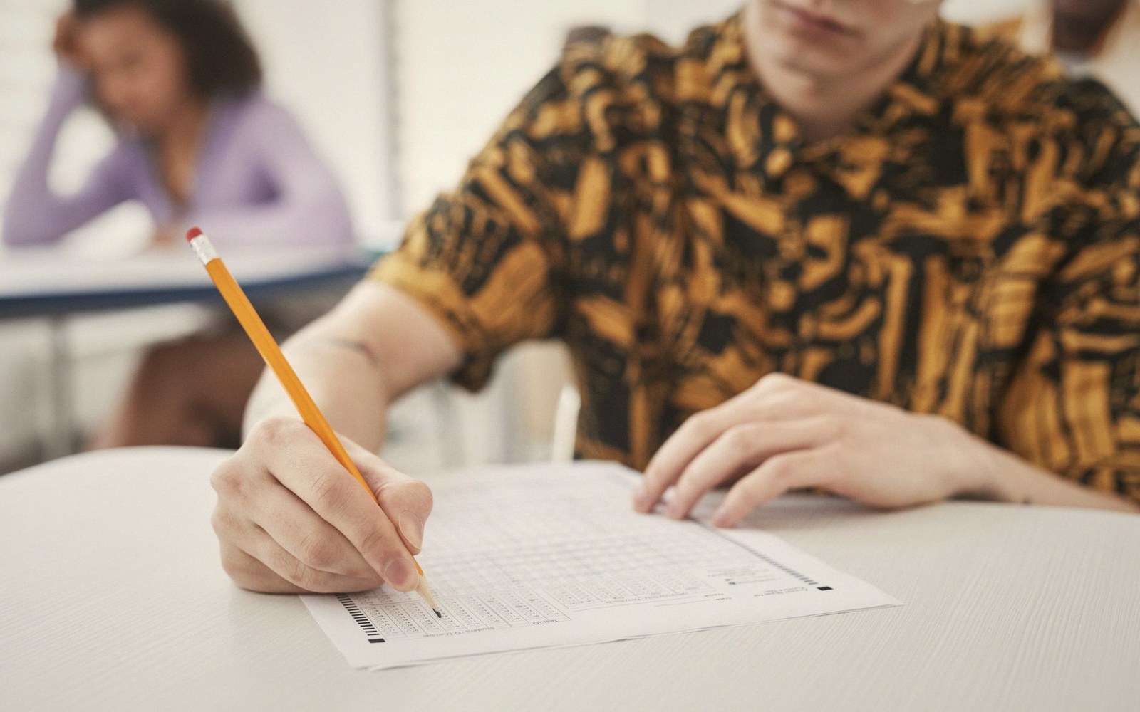 Student filling in a multiple-choice answer sheet with a pencil at a desk